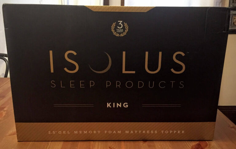 A black box with gold and white text reads "ISOLUS Sleep Products" with a 3-year warranty logo above. The word "KING" is written below, along with "2.5' Gel Memory Foam Mattress Topper." The mattress topper box is placed on a wooden surface.