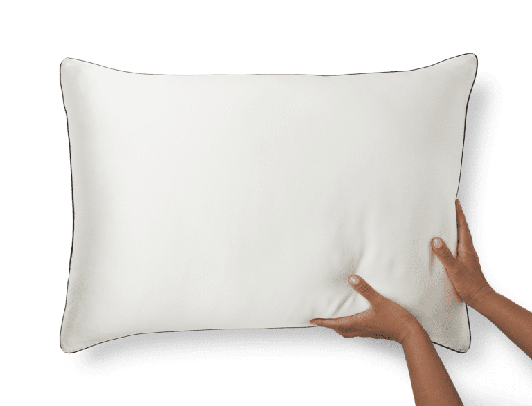 Two hands are shown adjusting or holding a white Silk Pillowcase against a black background. The pillowcase is rectangular and appears to be soft and plush.