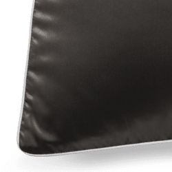 A close-up shot of a black Silk Pillowcase with elegant white piping along its edges. The fabric boasts a smooth and glossy texture, and the seam along the piping is clearly visible. The lighting accentuates the luxurious quality of the pillowcase's material.