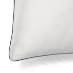 A close-up image of the Silk Pillowcase, showcasing its smooth white fabric with a dark border on one side. The pillowcase features a rounded corner, and the focus is on the texture and finish of the luxurious silk material, with the background in shadow.