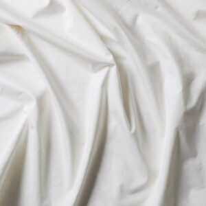 A close-up of white, crumpled fabric. The surface appears soft with multiple folds and creases, suggesting a lightweight, possibly cotton or linen material. The texture and shadows give dimension to the fabric's smooth, plain appearance.