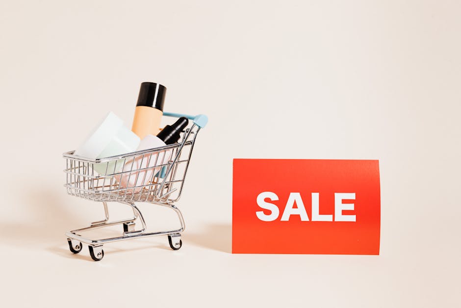 A miniature shopping cart filled with various cosmetics stands against a beige background. Next to the cart is a bright red sign with the word "SALE" in white letters.