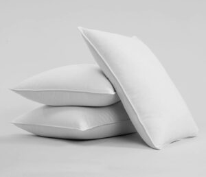 Three white pillows are stacked together against a plain background. Two of the pillows are laid flat one on top of the other, and the third pillow is propped up at an angle on top of the other two. The overall appearance conveys a clean and pristine look.