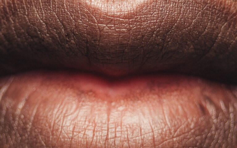 Close-up of a person's lips, showing detailed textures and natural lines on the upper and lower lips. The lighting highlights the contours and natural color variations on the skin.