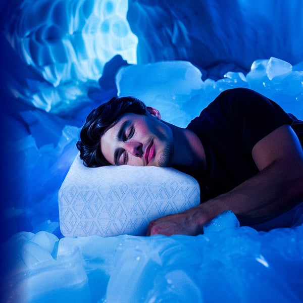 A person is lying on their side, resting their head on a white pillow with a geometric pattern. The background and surroundings are filled with blue-tinted ice, creating the appearance of an icy, ethereal environment. The overall mood is calm and serene.