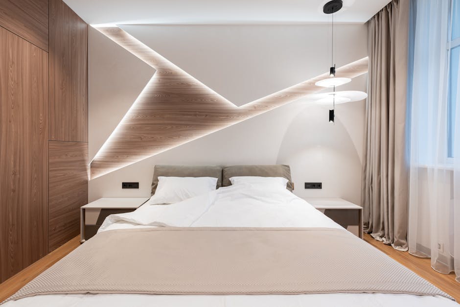 Modern bedroom with a double bed featuring white and beige bedding. There are two wooden nightstands, each with a black lamp. The unique wooden headboard has integrated lighting, creating geometric patterns. A curtain covers a window on the right side of the room.