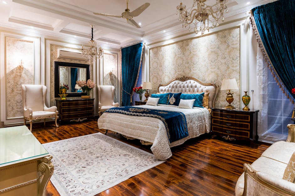 Luxurious bedroom with a large bed adorned with blue and white bedding, ornate chandeliers, dark wooden furniture, and richly designed wallpaper. The room features elegant armchairs, a plush rug, navy curtains, and decorative lighting, exuding opulence and comfort.