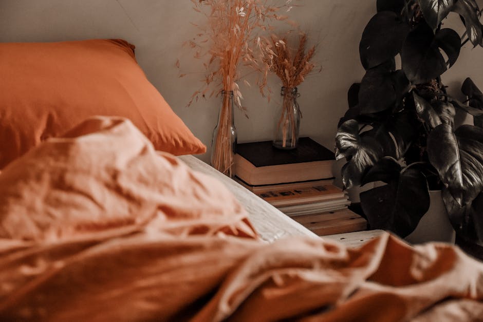 a bed with orange sheets and a vase of dry grass