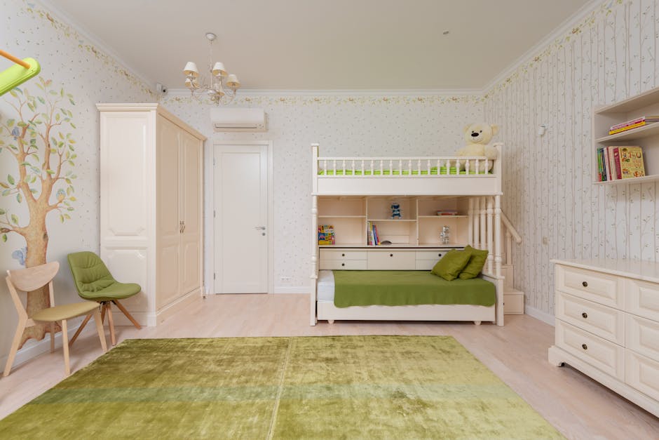 A neatly arranged children's room with a loft bed. The lower bed has green bedding, and the room features green-themed decor, including a green rug and chairs. There are shelves, a wardrobe, and a dresser. The wall has a tree mural with bookshelves.