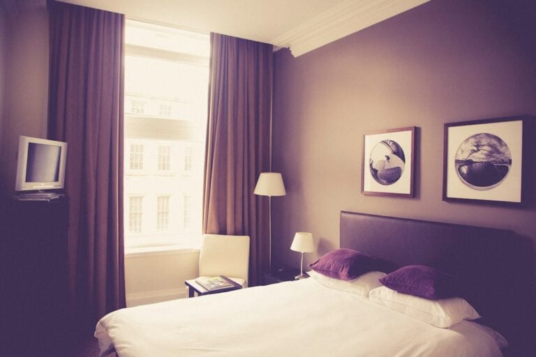 a bed with purple pillows and a lamp next to a window