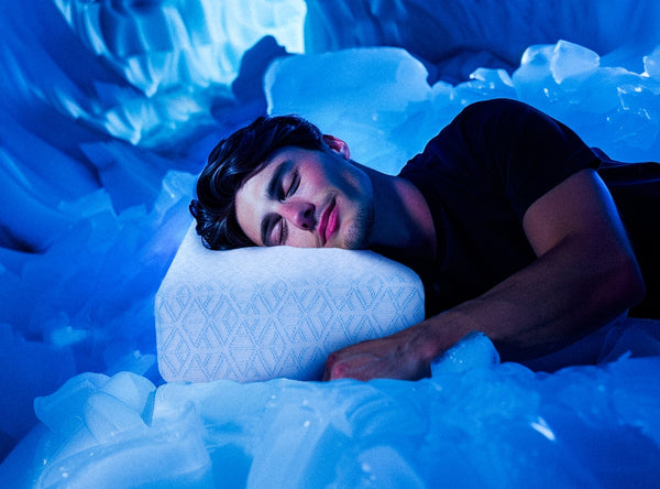 A person is sleeping peacefully on a white pillow surrounded by a surreal, icy blue environment. The dim blue lighting creates a serene, dreamlike atmosphere. The individual appears relaxed and content, with a slight smile on their face.