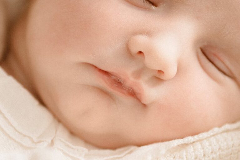 Close-up of a sleeping baby's face. The baby has closed eyes and a serene expression, with soft features and delicate skin. The image captures the tenderness and peacefulness of the sleeping infant. The baby is wearing a light-colored garment.