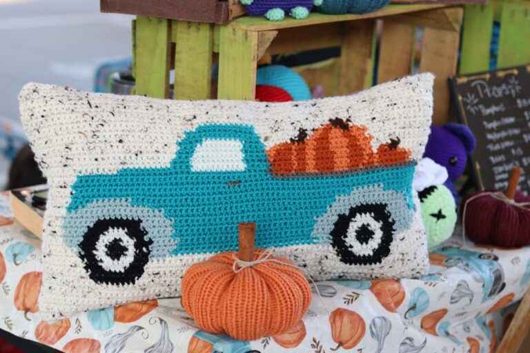 a knitted pillow with a truck and pumpkins on a bed