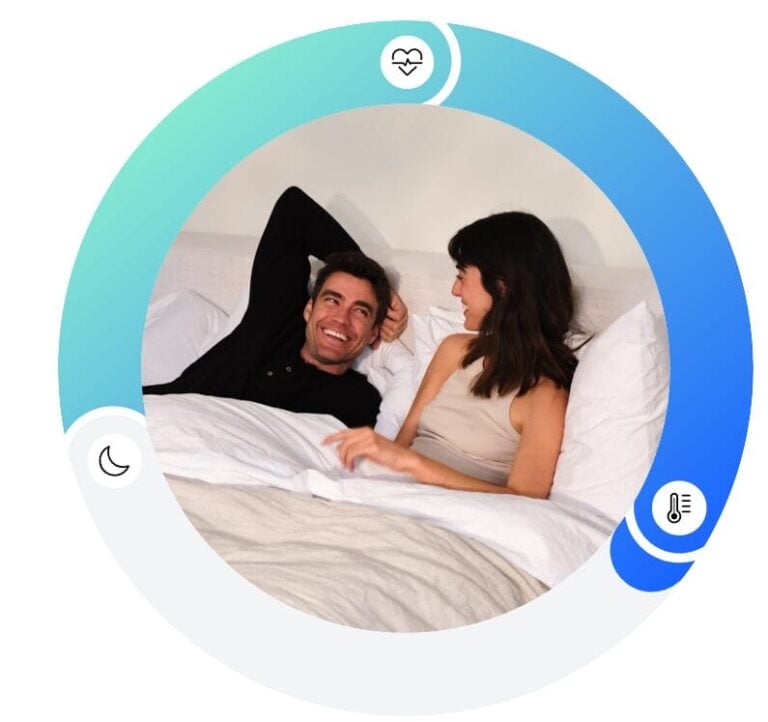 A man and a woman lie in bed, smiling and looking at each other. They are surrounded by a circular graphic with icons representing heart health, sleep, and temperature. The background transitions from light blue to dark blue.