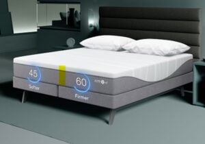 A modern bed with dual firmness settings is shown in a stylish bedroom. The left side is labeled "Softer" with a firmness level of 45, and the right side is labeled "Firmer" with a firmness level of 60. Two pillows are placed on the bed, and the room features contemporary decor.