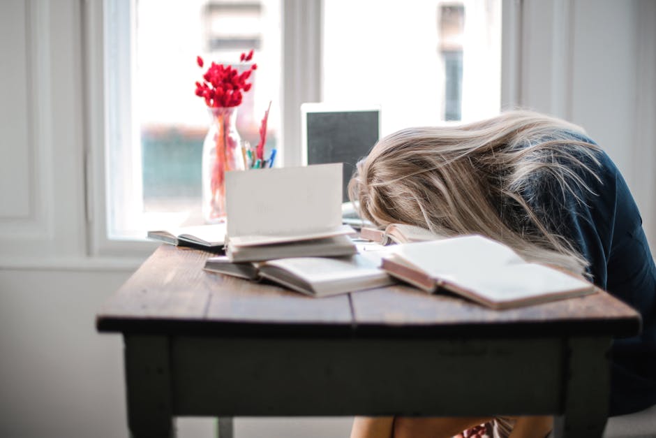 a woman with her head on a desk with books