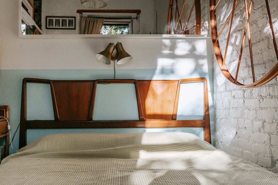 a bed with a white blanket and a white wall with a light on the wall