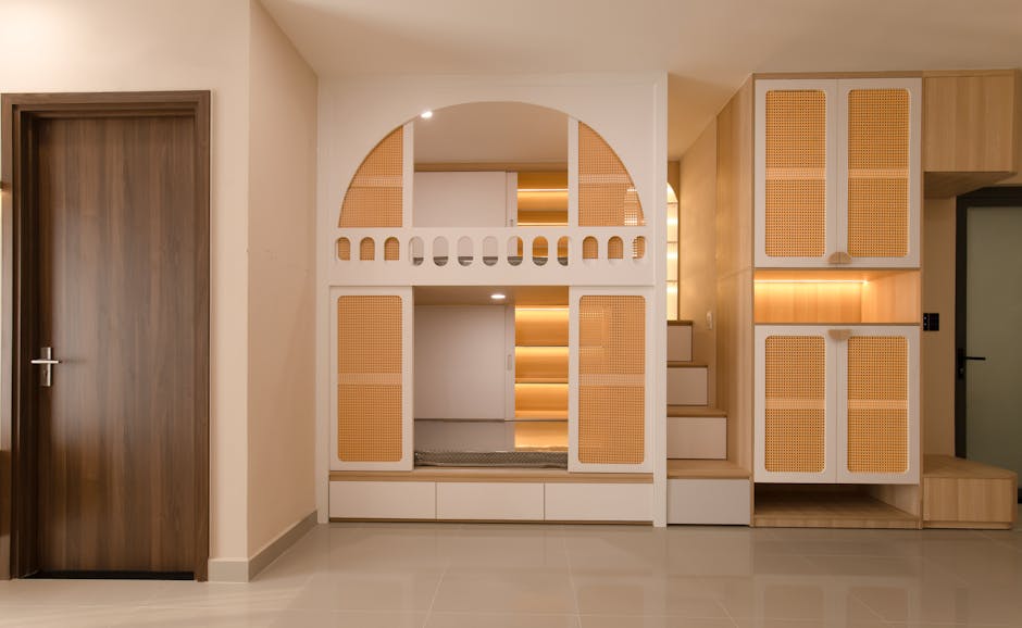 A modern, minimalist bedroom featuring a built-in bunk bed with an arch design. The lower bunk is enclosed with doors, and the upper bunk is accessible by stairs with cabinets under each step. The warm-toned wooden elements and soft lighting create a cozy ambiance.