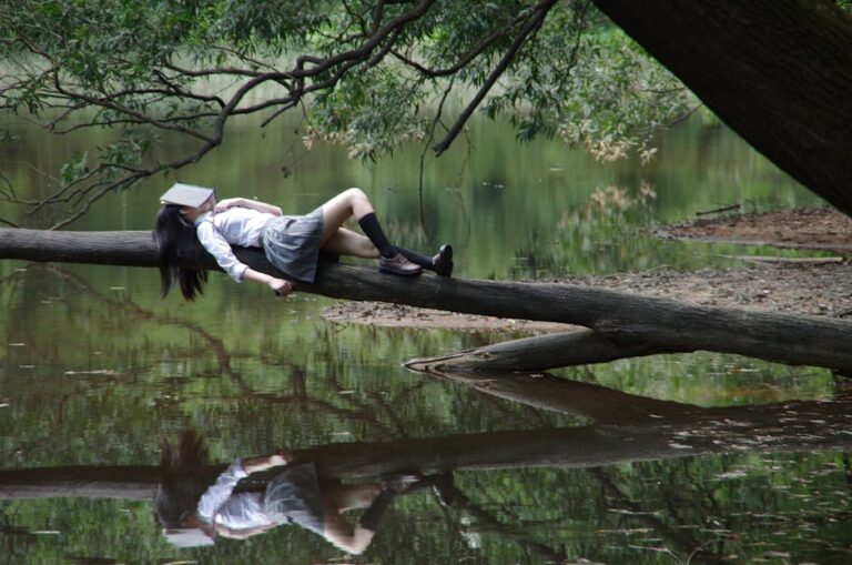 a woman lying on a log with a book on her head