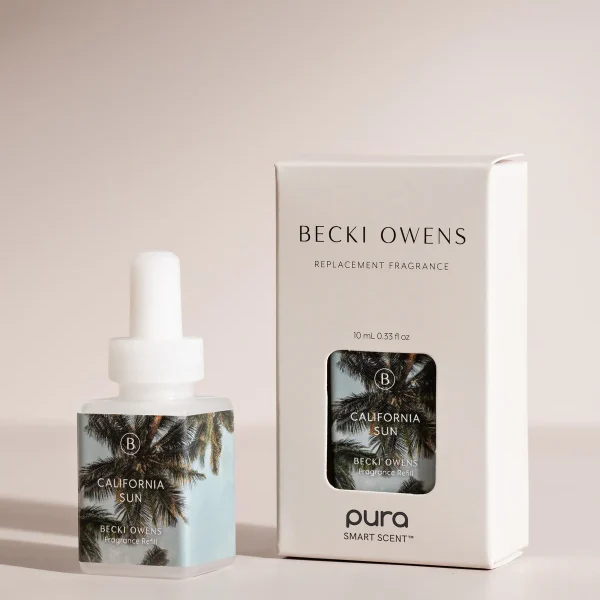 A bottle and box of the "California Sun" fragrance by Becki Owens for Pura. The label displays an image of palm trees against a clear sky, and the white box with black text includes cut-out windows that showcase the bottle.