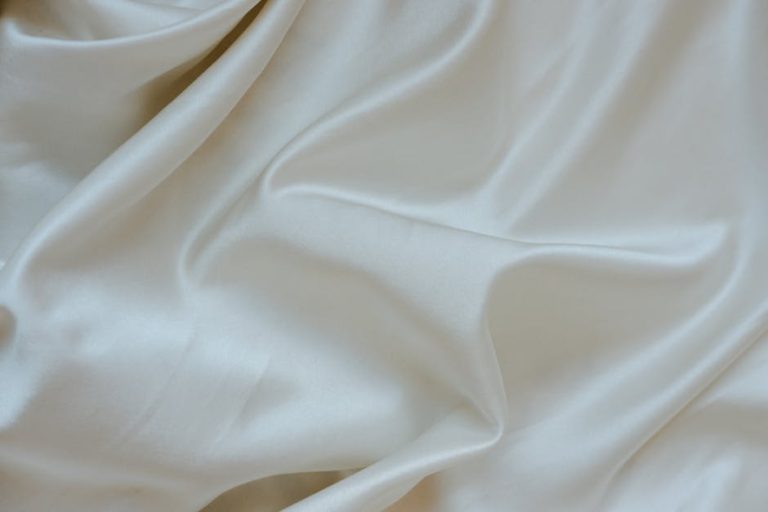 A close-up view of smooth, cream-colored fabric with soft folds and a silky texture, creating an elegant and luxurious appearance.