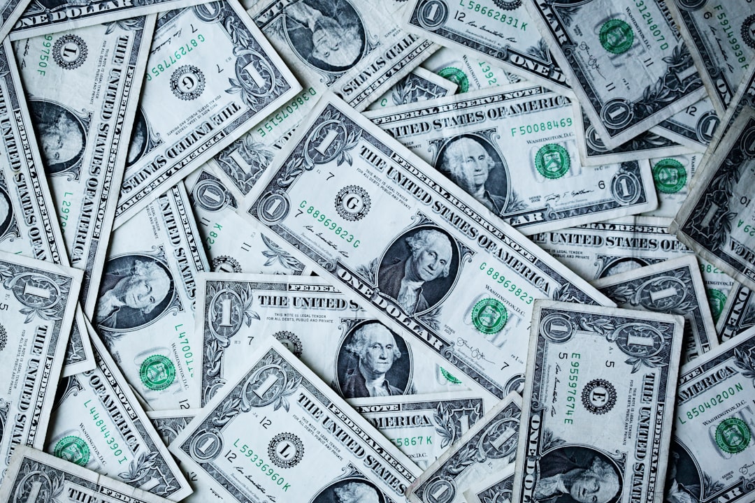 A scattered pile of U.S. one-dollar bills, featuring the portrait of George Washington. The bills are spread in various angles, creating a textured pattern of currency.