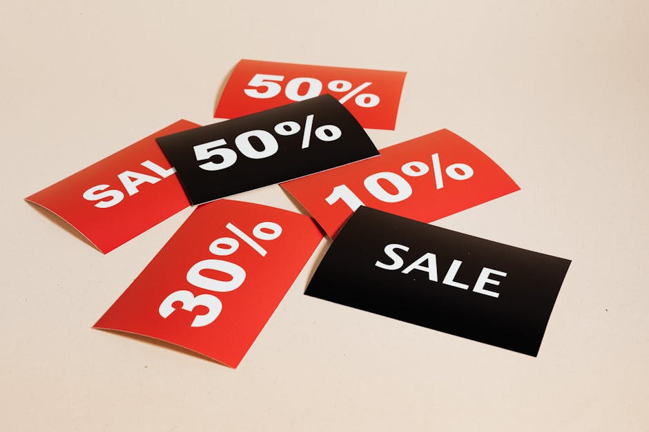 Red and black sale signs scattered on a surface. The red signs display "SALE," "50%," "10%," and "30%," while the black sign reads "SALE.