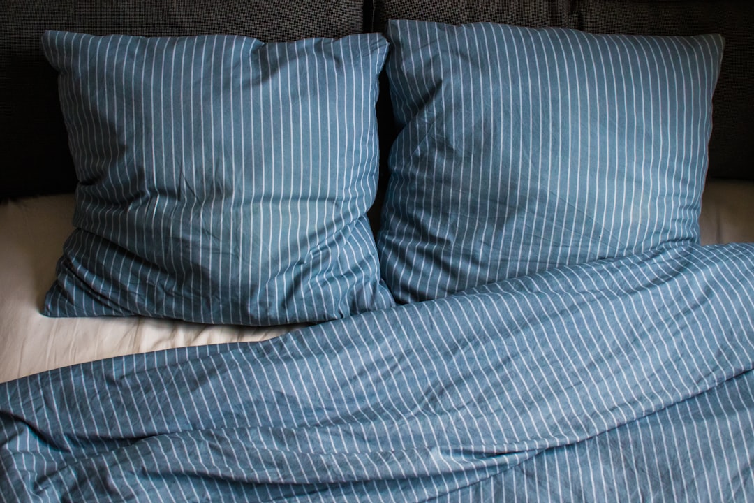 Two pillows and a comforter with blue and white vertical stripes are neatly placed on a bed. The background features a dark headboard, adding contrast to the bedding.