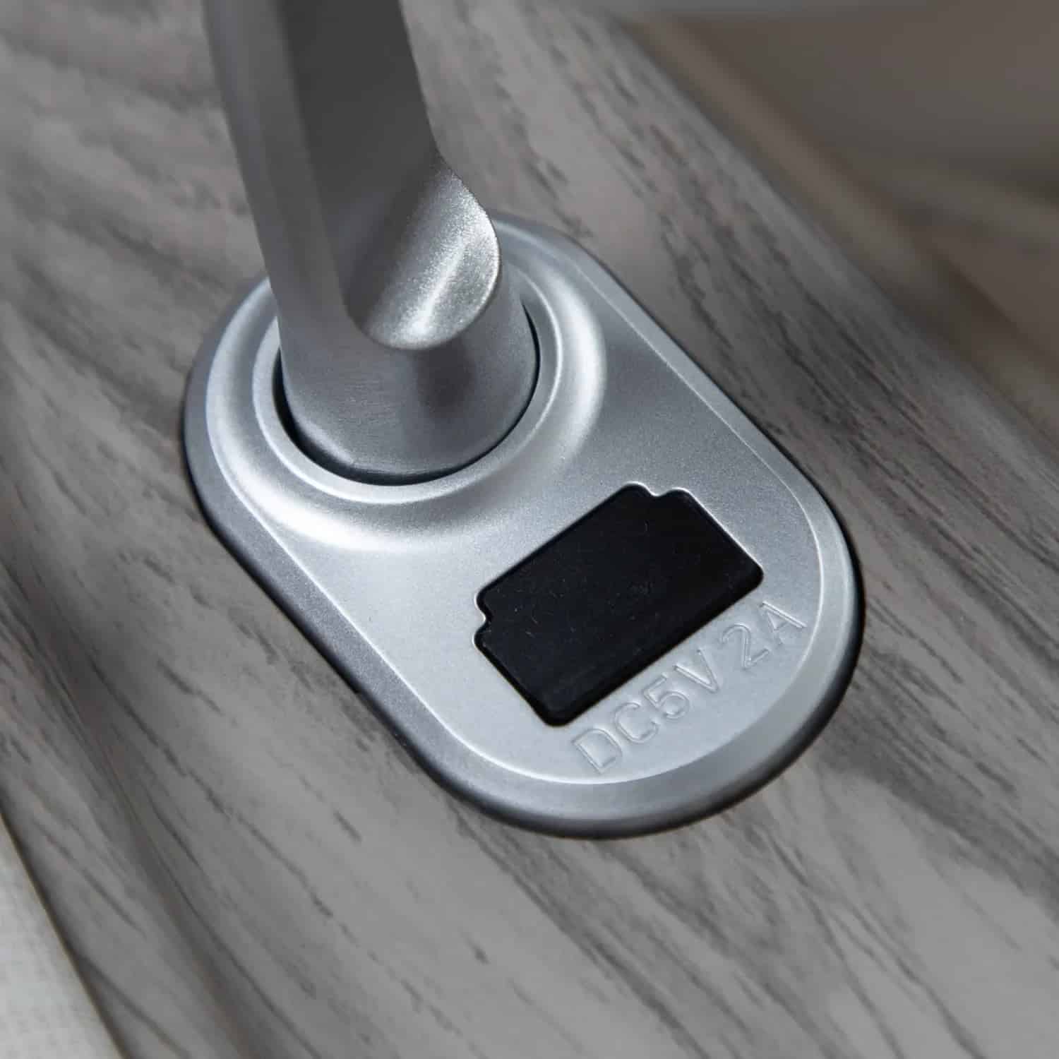 Silver gray swivel joint with embossed text "DC5V 2A" on a light wood surface