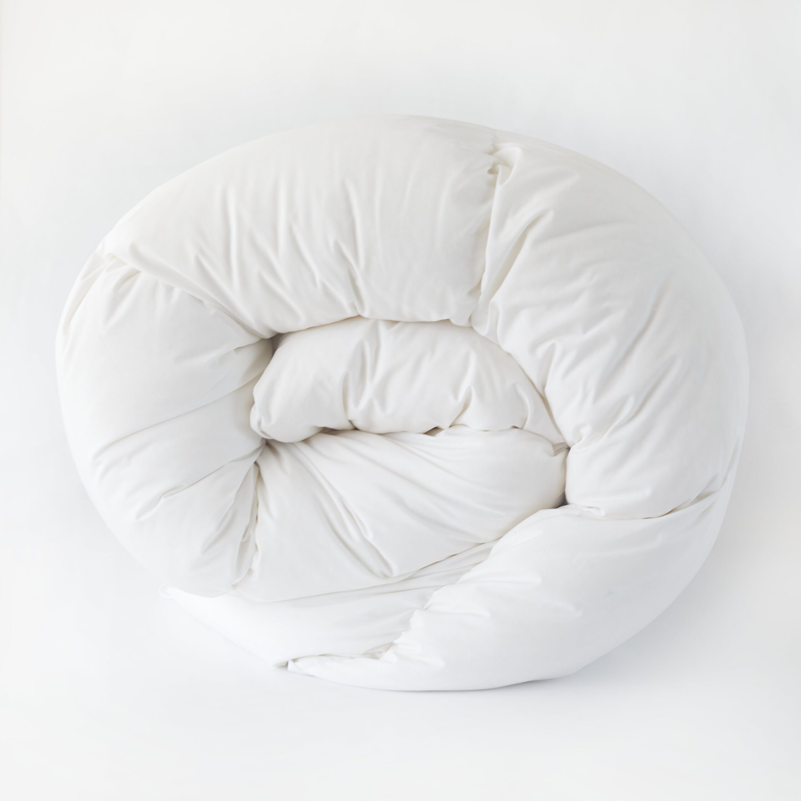 Rolled white All Season Comforter on a neutral background, showing its fluffy texture.