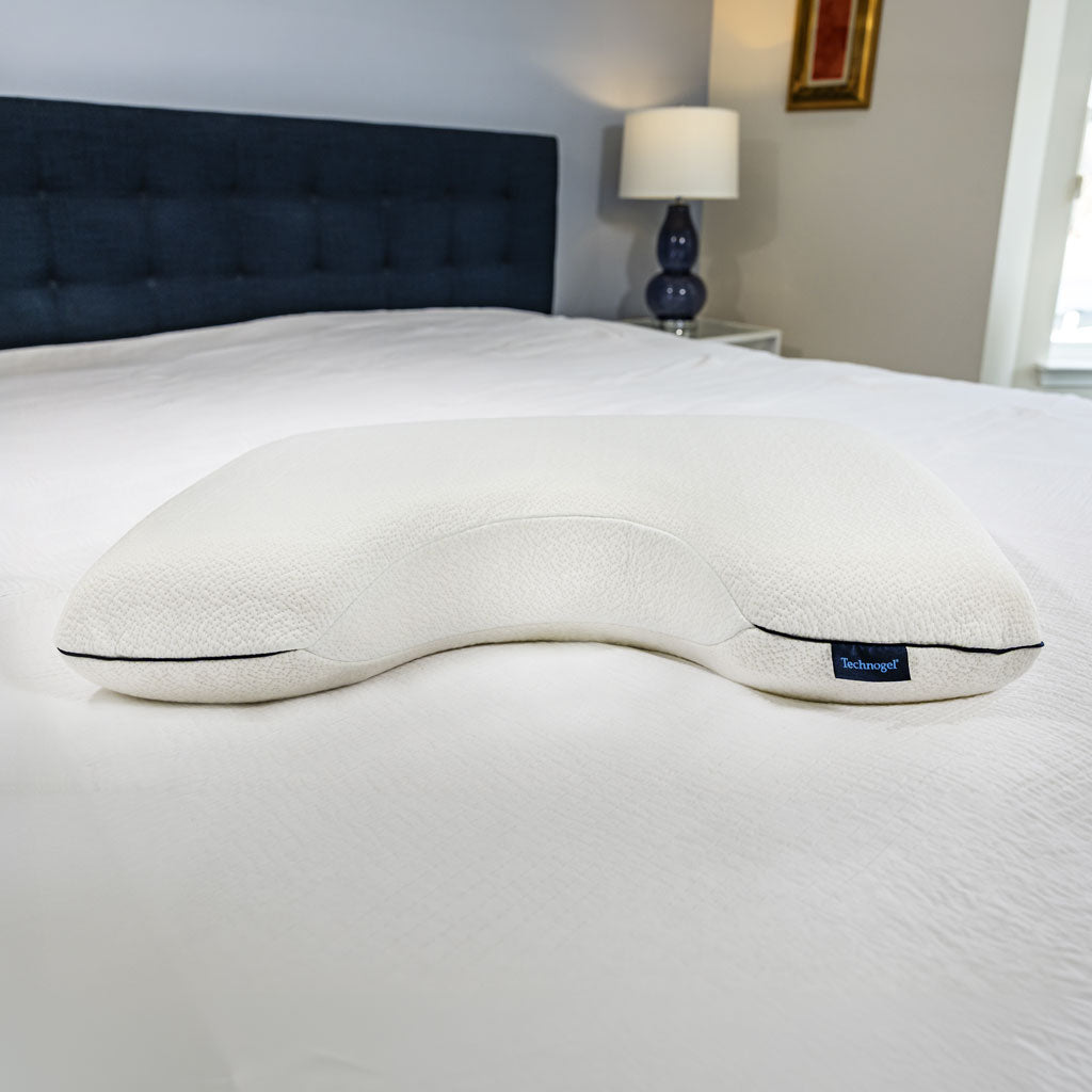 White Technogel Side Sleeper Pillow with blue seams on a bed with a dark blue headboard