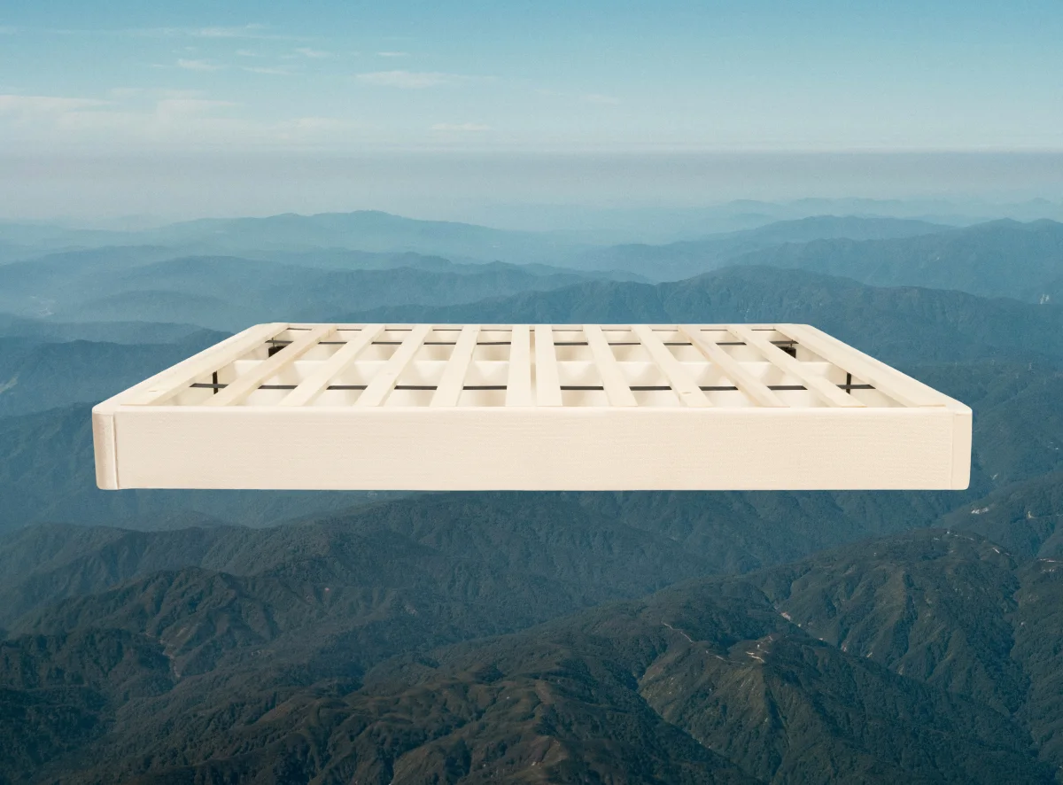 Light beige wood foundation box spring with black slats floating above mountain range