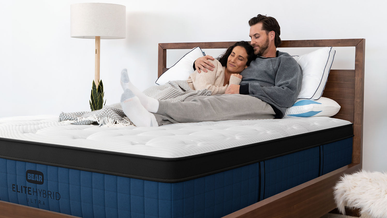 Couple cuddling on the white and blue EliteUltraHybrid mattress in a dark wood bed frame
