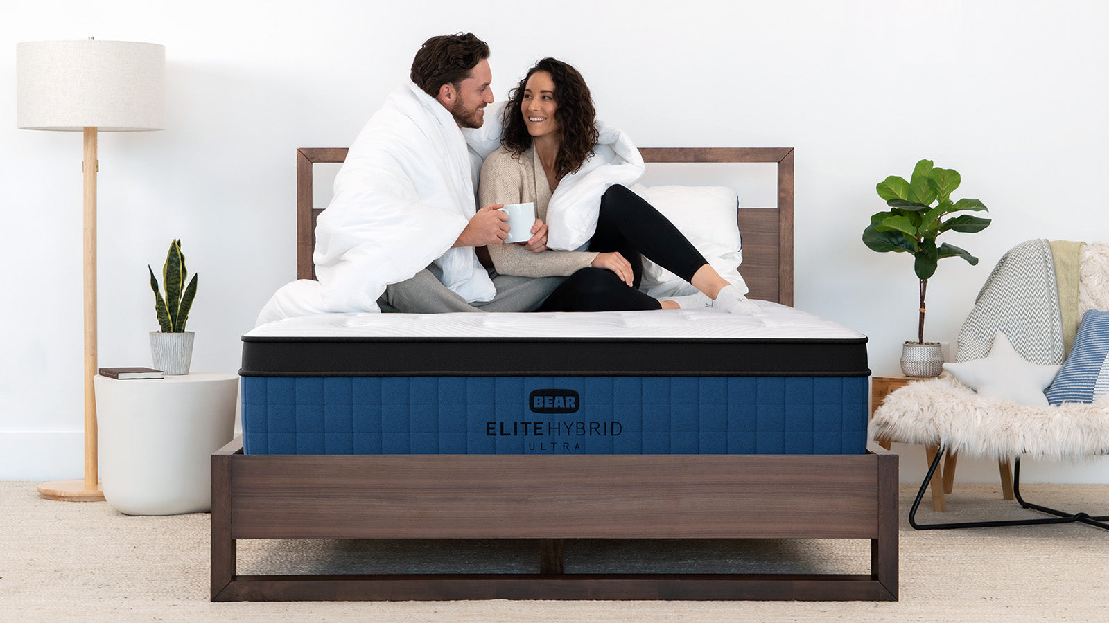 Couple sits bundled in a white comforter on Bear Elite Hybrid mattress.