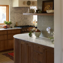 Warm kitchen with marble countertops, wooden cabinets, and a white smart diffuser plugged into a wall outlet