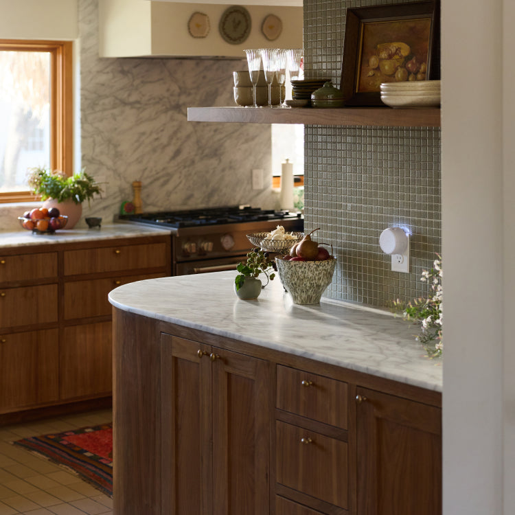 Warm kitchen with marble countertops, wooden cabinets, and a white smart diffuser plugged into a wall outlet