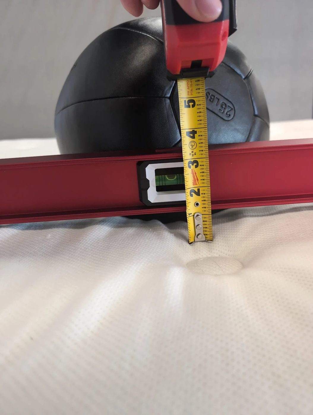 Tape measure showing sinkage depth under a 25 lb medicine ball on the WinkBed mattress next to a level