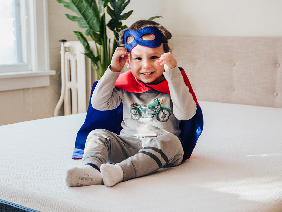 Kid smiles wearing superhero cape and mask