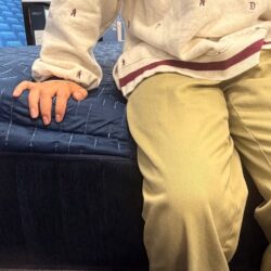 Tester sitting on the side of a blue quilted hybrid mattress evaluating edge support compression.
