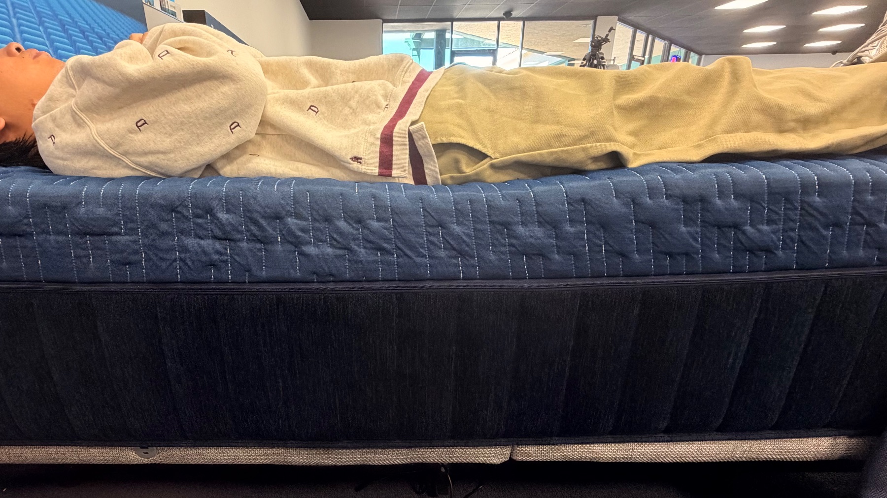 Tester lying on their back directly along the edge of a blue quilted mattress.