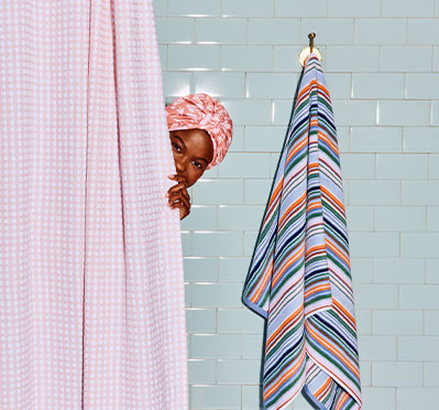 Pink gingham shower curtain and striped bath towel shown by HomeGoods