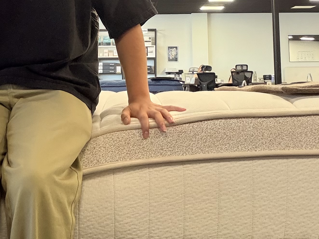 Tester sitting on the perimeter of a hybrid mattress to evaluate edge sinkage and firmness.
