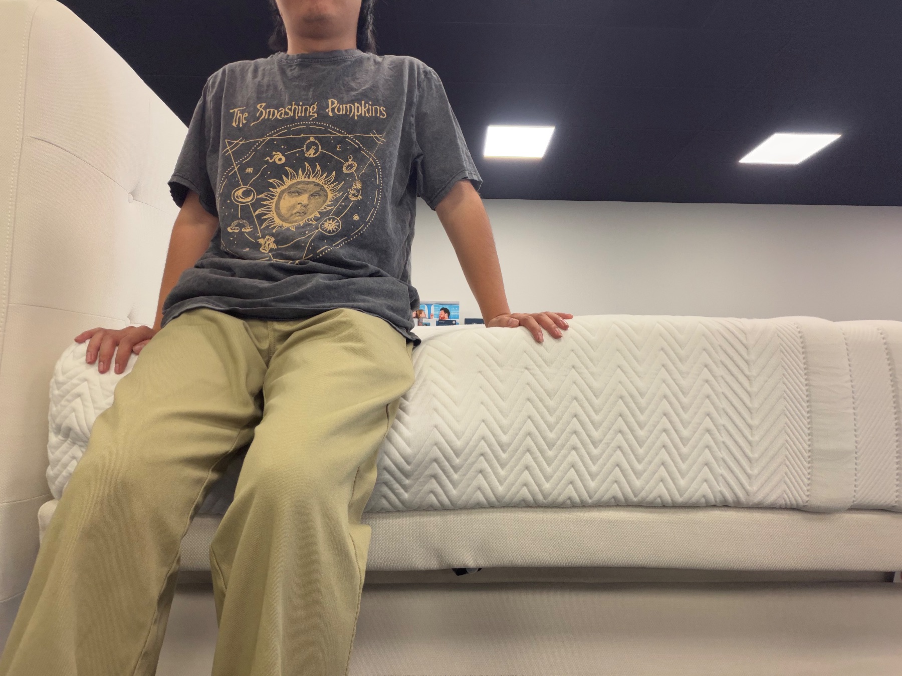 Person sitting directly on the edge of a white mattress to test perimeter sinkage and support.