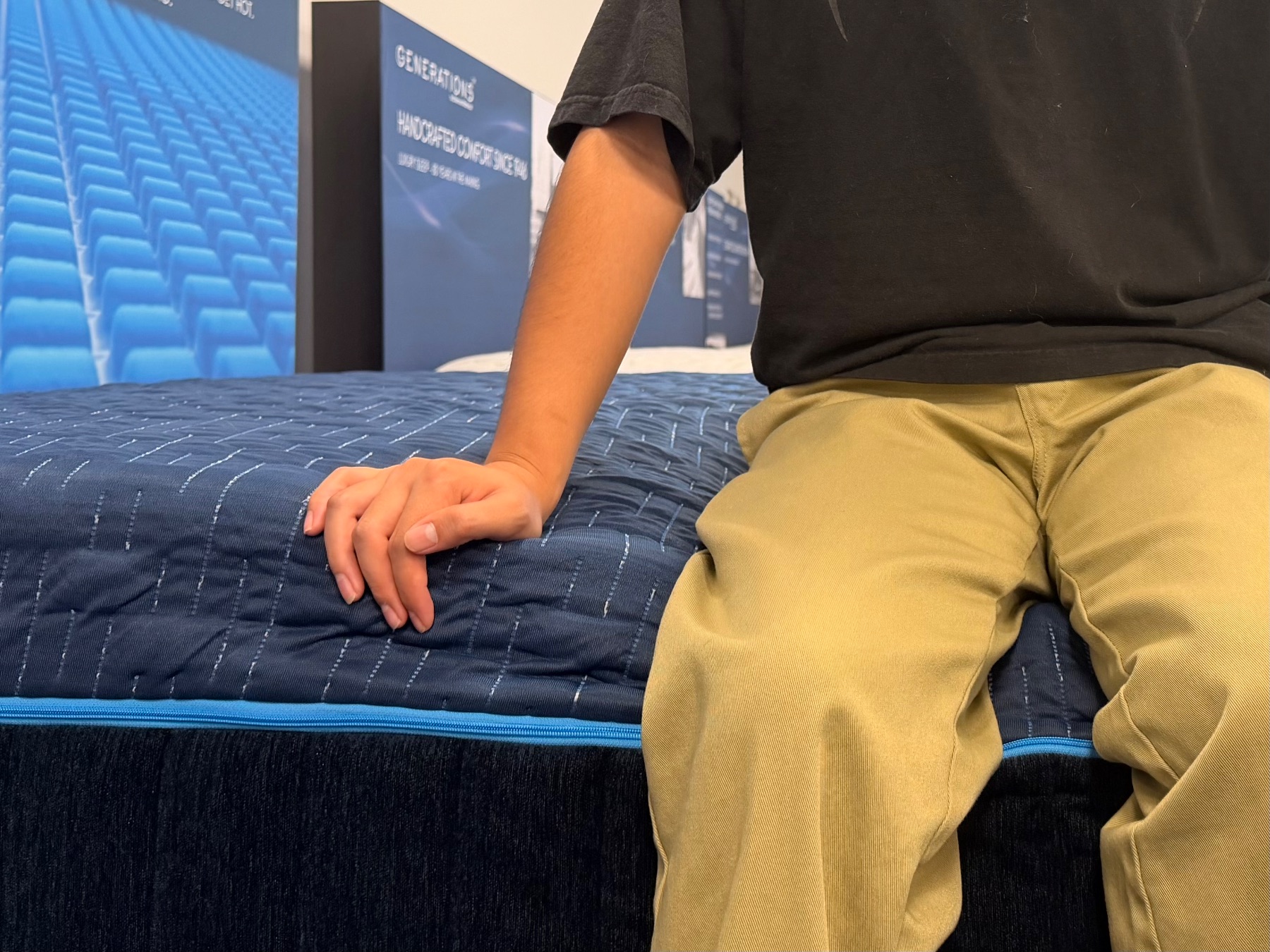 Person sitting directly on the blue quilted edge of a mattress to test edge support.