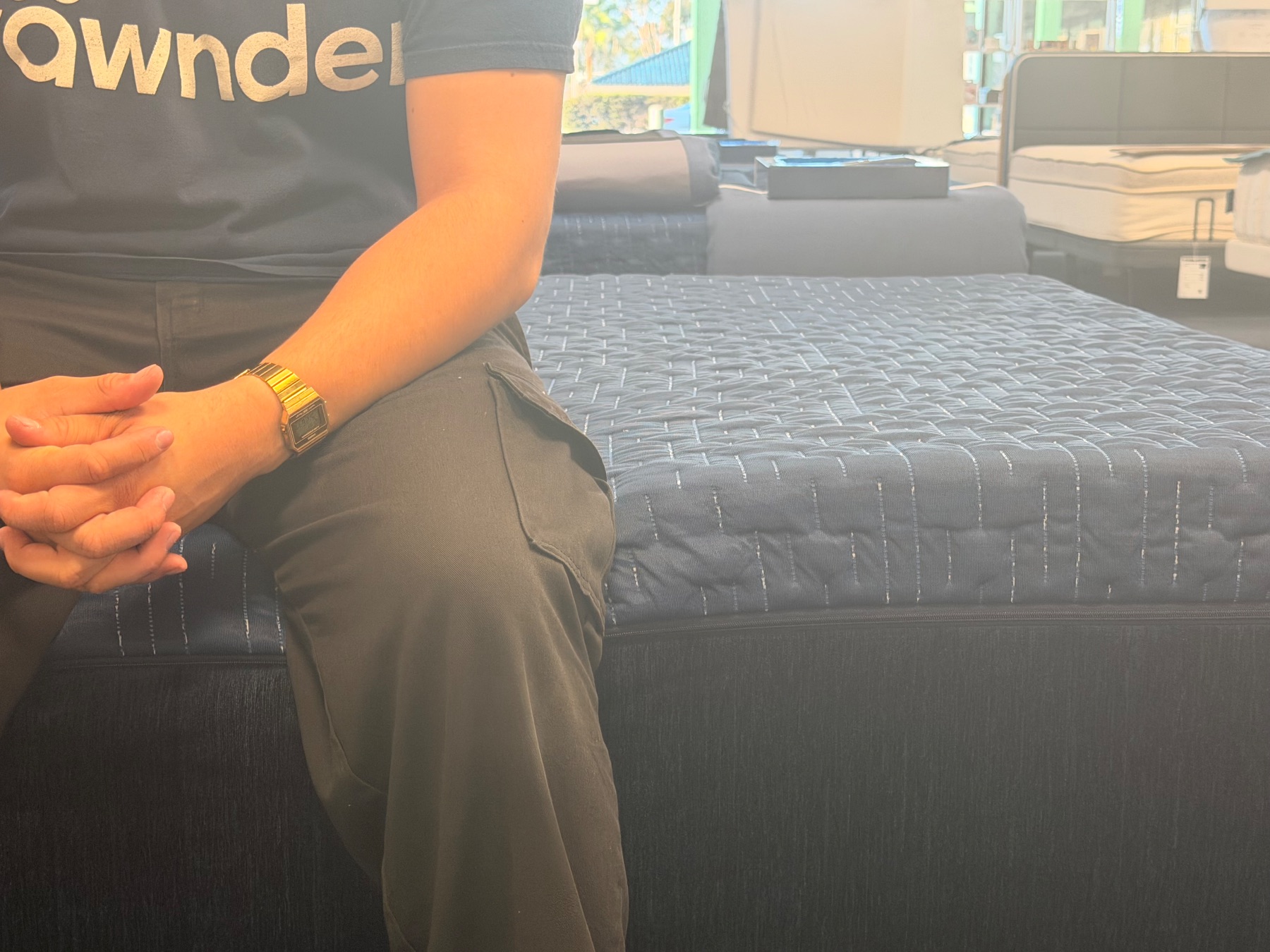 Reviewer sitting on the edge of a dark blue quilted Technogel mattress during an edge support evaluation.