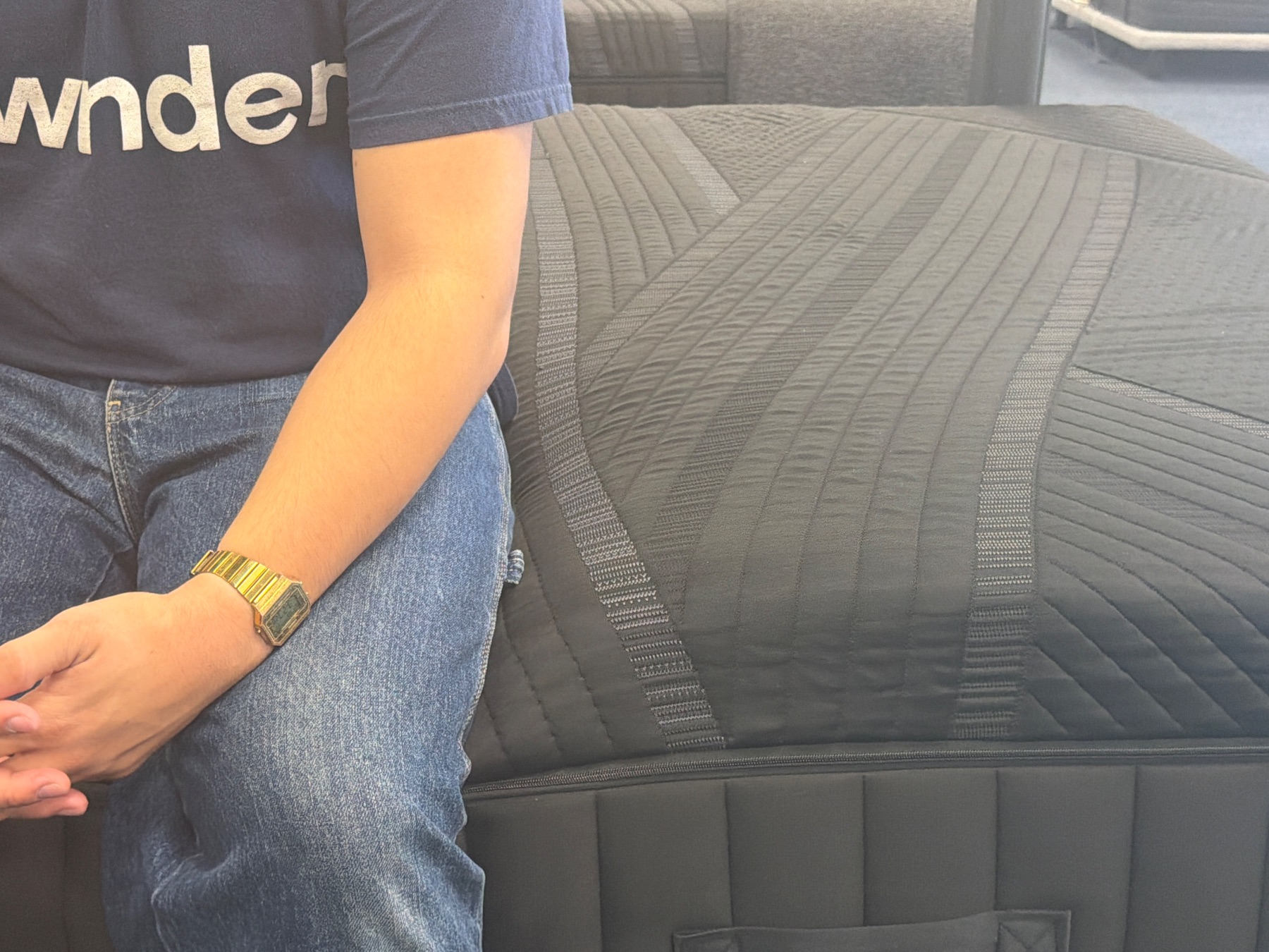 Reviewer sitting on the edge of a dark hybrid mattress to evaluate edge compression.