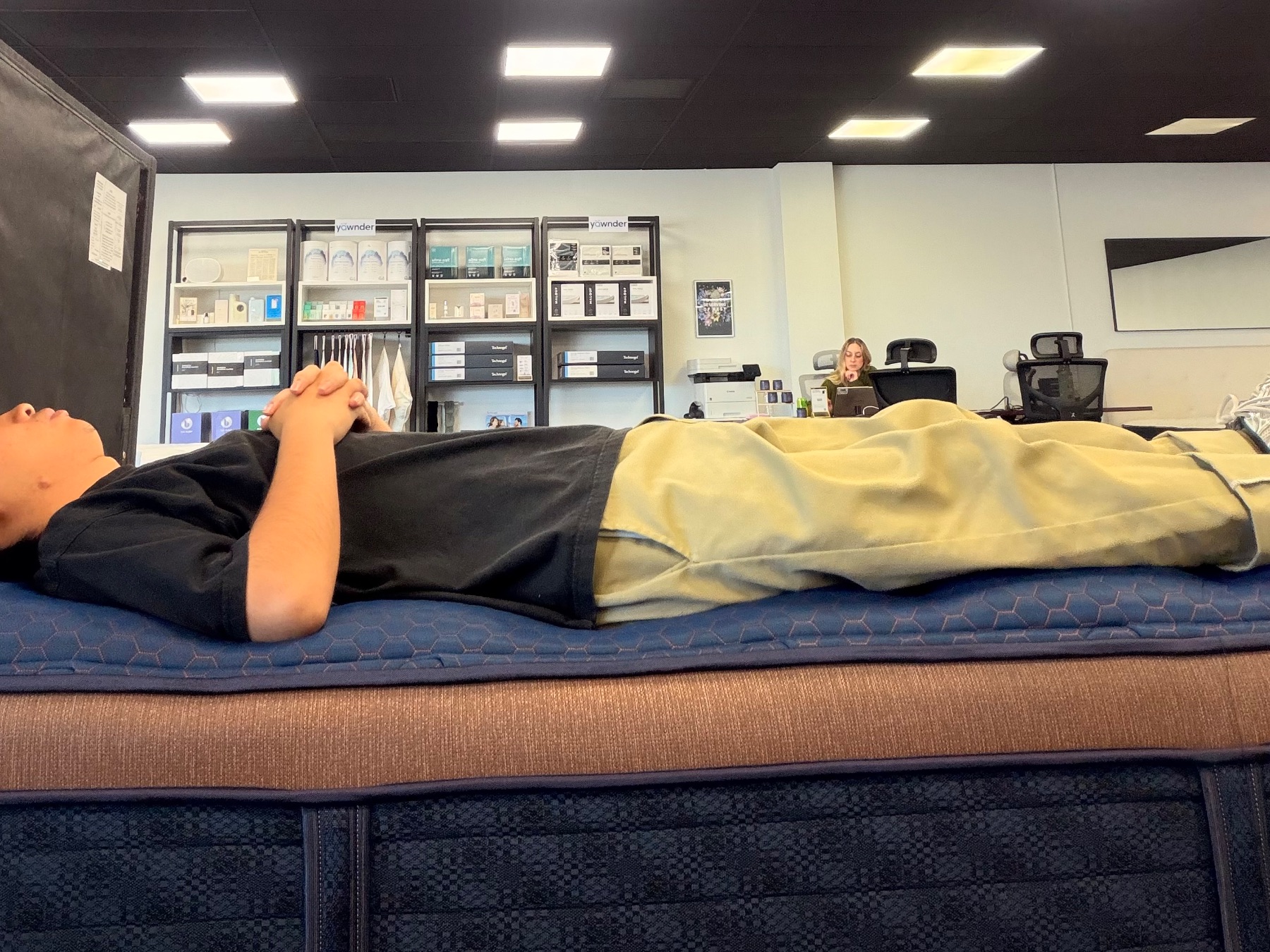 Tester lying on their back directly along the edge of a blue and brown mattress to test edge support.