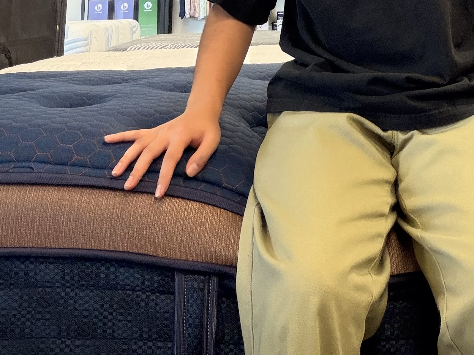 A person sitting on the edge of a mattress testing perimeter support and sinkage.