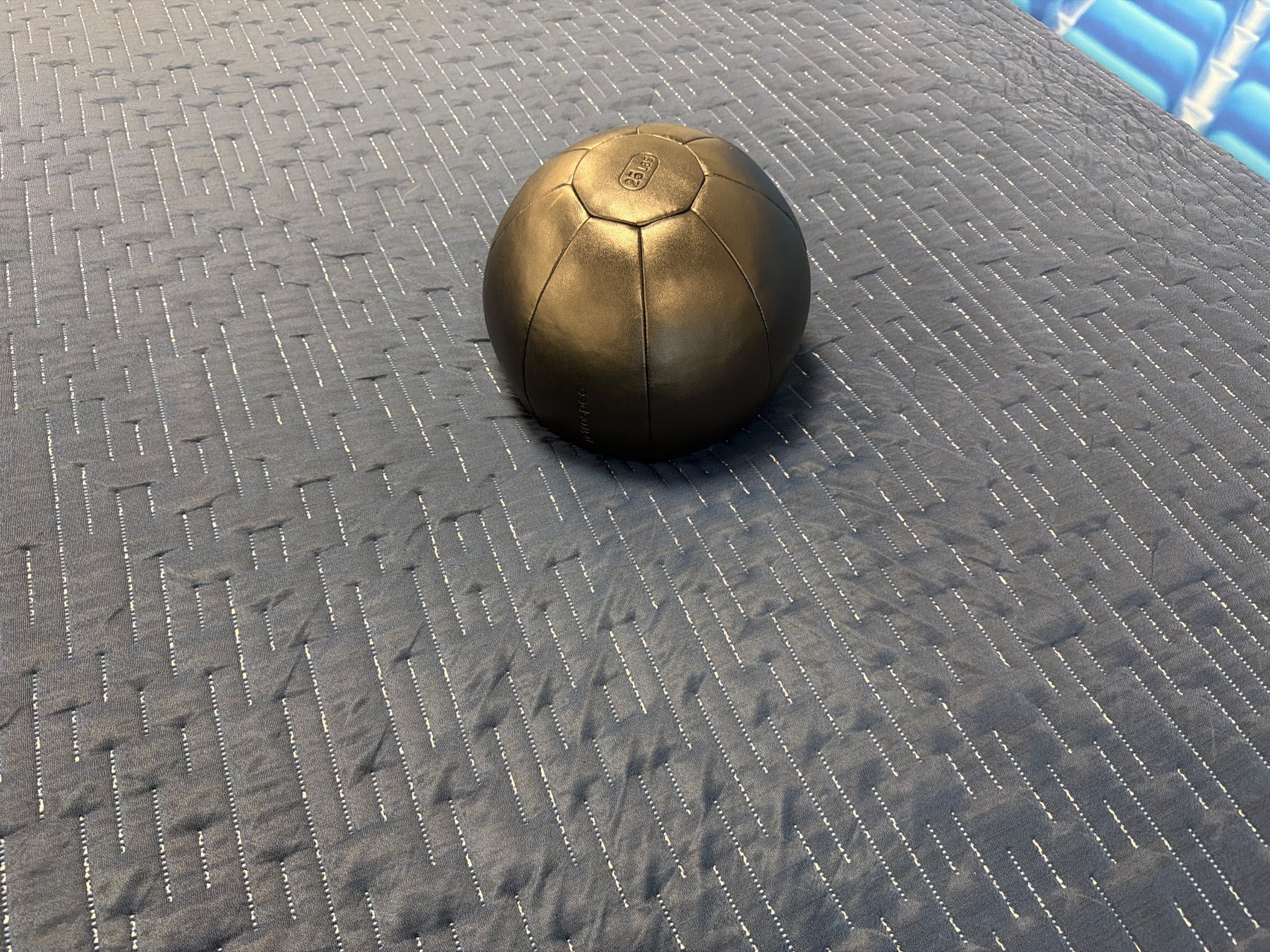 A 25 lb weighted ball resting on a blue textured mattress surface to measure sinkage.