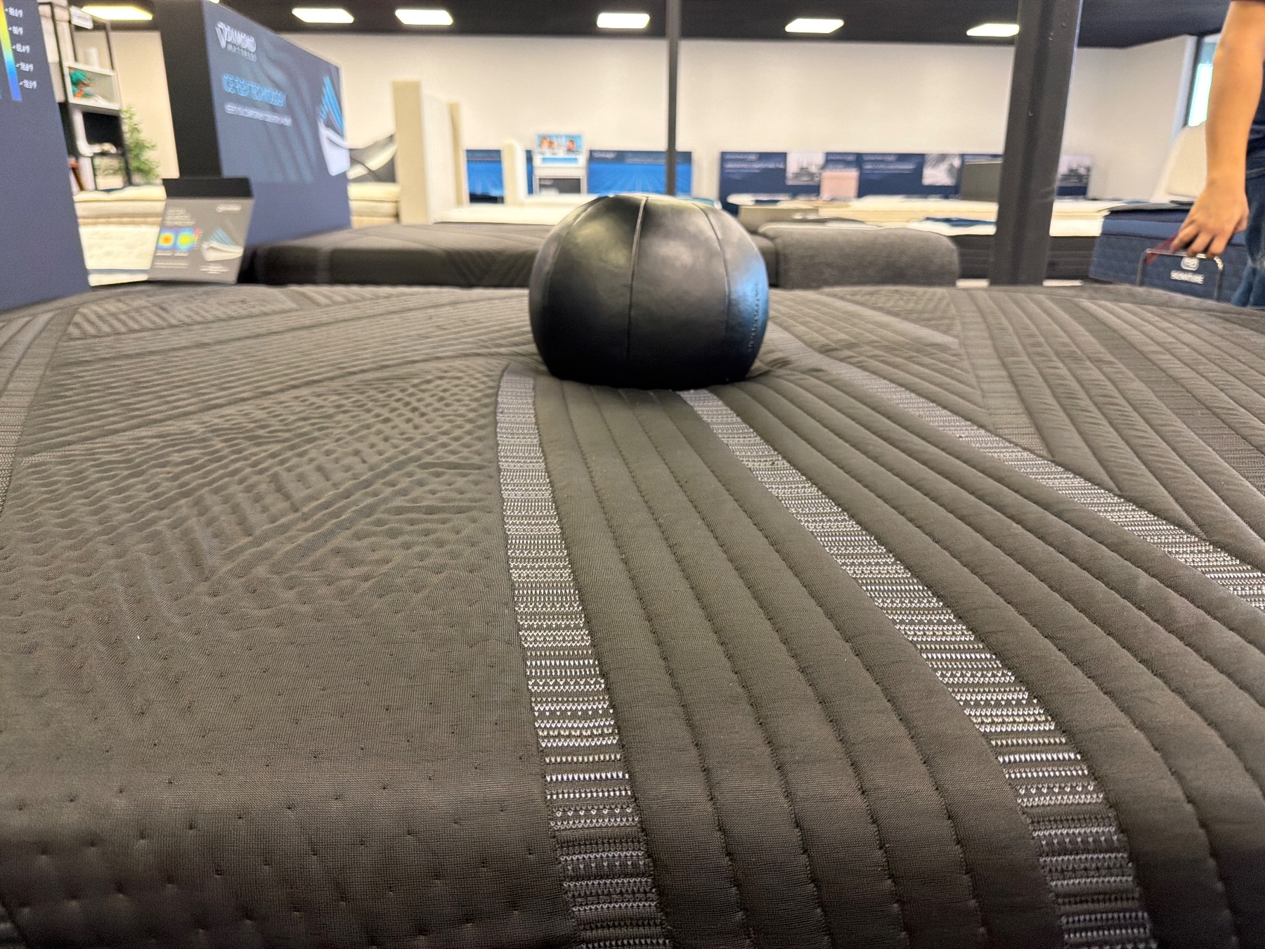 Weighted black ball resting on a dark quilted mattress to test sinkage depth.